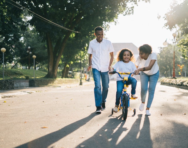 Dad and Mom with daughter teaching to ride bike - family life insurance